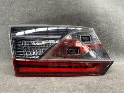 Automotive tail light assembly with a red lower lens and clear upper section on a dark background.