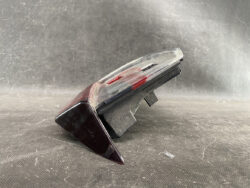 Close-up of a black cassette tape with a clear cover, lying on its side on a dark, textured surface, with red tape visible inside.