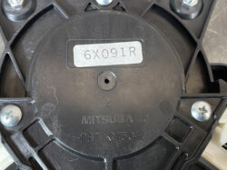 Circular Mitsuba plastic housing with part number 6X091R and 'PBT-GF30' engraving on the bottom plate, showing screws and mounting holes.