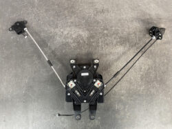 Dual-cable linkage assembly with a central black housing and two long cables extending to pedal ends, laid on a gray workshop floor.