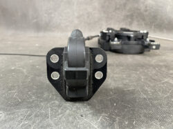 Close-up of a black roller hinge with a central wheel and four mounting holes on the sides, resting on a textured surface.